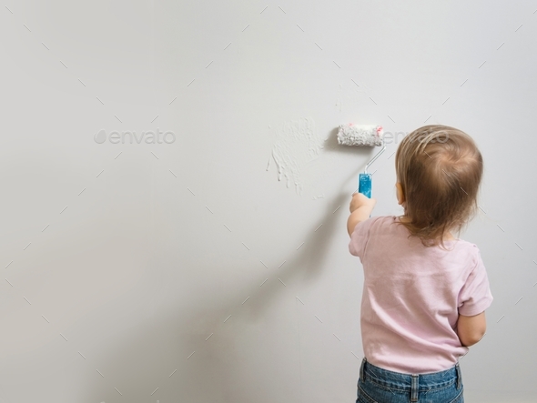 Little child painting the wall with roller and light gray paint, empty background. Interior decorati