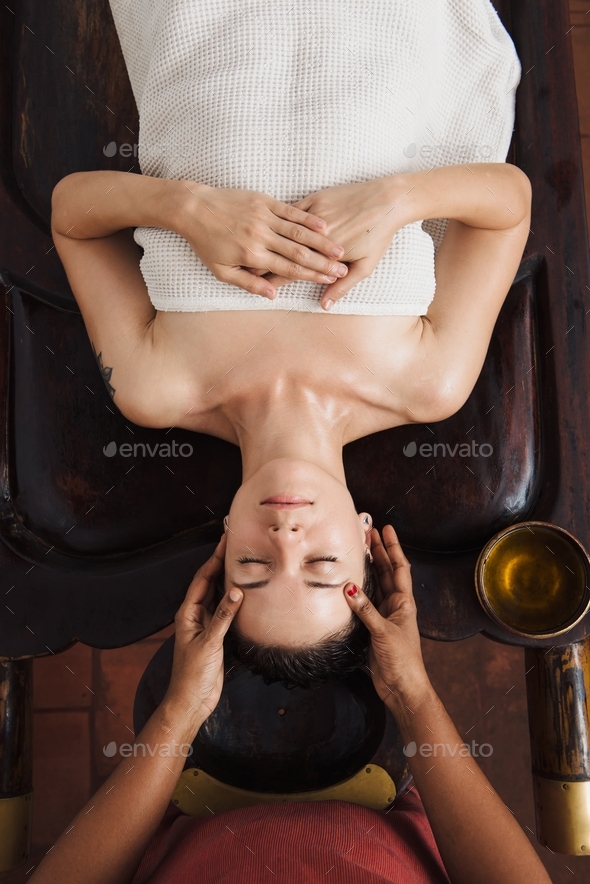 Ayurvedic face massage with oil on the wooden table in traditional style made by asian women. Top vi