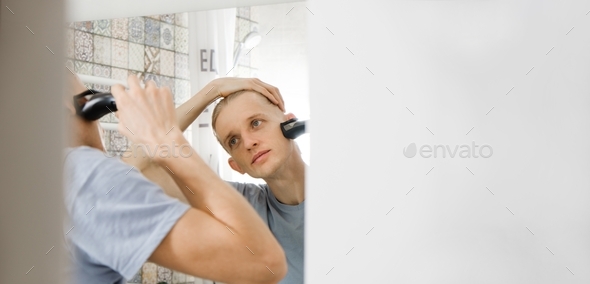 Man shaving whiskers hair by electric razor by himself at home