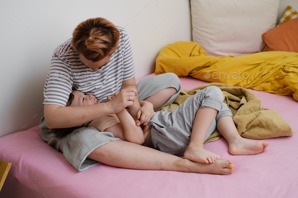 Mother tickling child in bed, playing in the morning