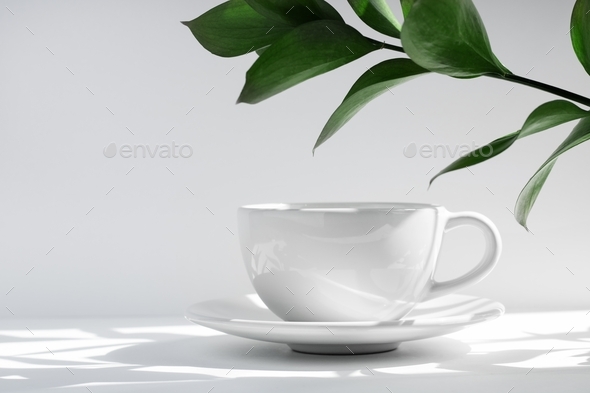 White tea or coffee mug and saucer, on a white table in the rays of the sun, with hard shadows
