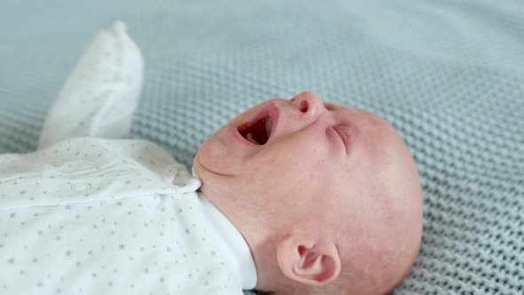 close-up baby screams strongly while lying on the bed