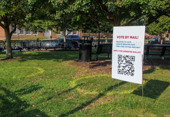 A vote by mail sign with barcode at a college park marked with social distance small pods circles.