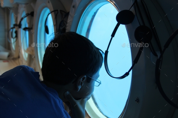 Teen in submarine under ocean observing the marine life through the window in Hawaii