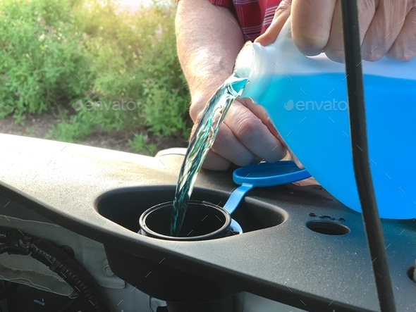 Windshield washer fluid being poured into a vehicle\'s storage tank or reservoir by car’s owner