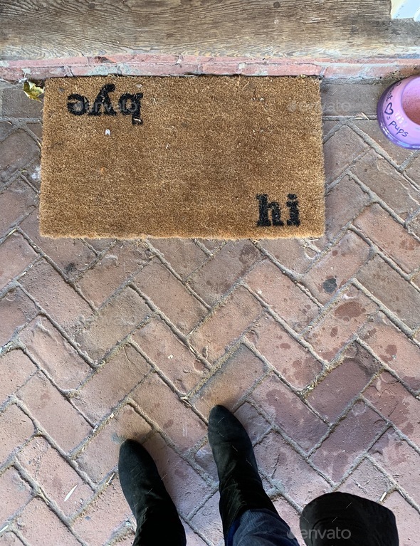 Hi bye home entrance rough doormat on brick floor with feet in view.