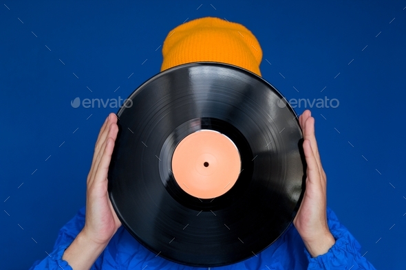 young man in a blue sport 90s style jacket and yellow hat holding vinyl record