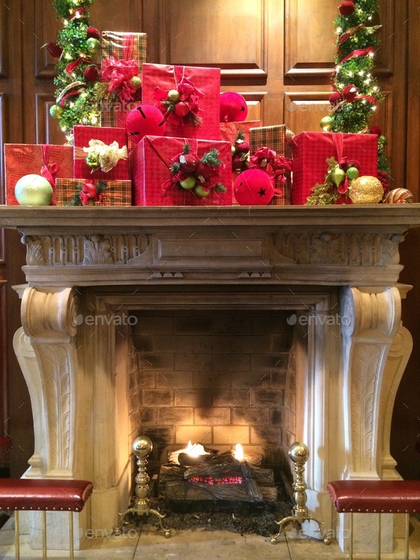 Fireplace mantel decorated with red Christmas presents & Christmas trees with lights & colors