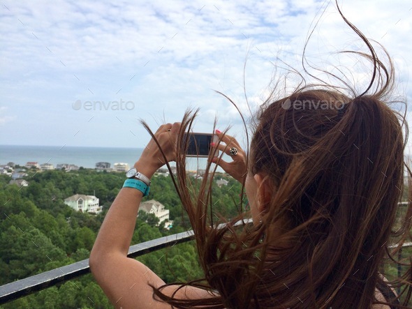 Young woman snapping photos at the top of a lighthouse on a very windy day