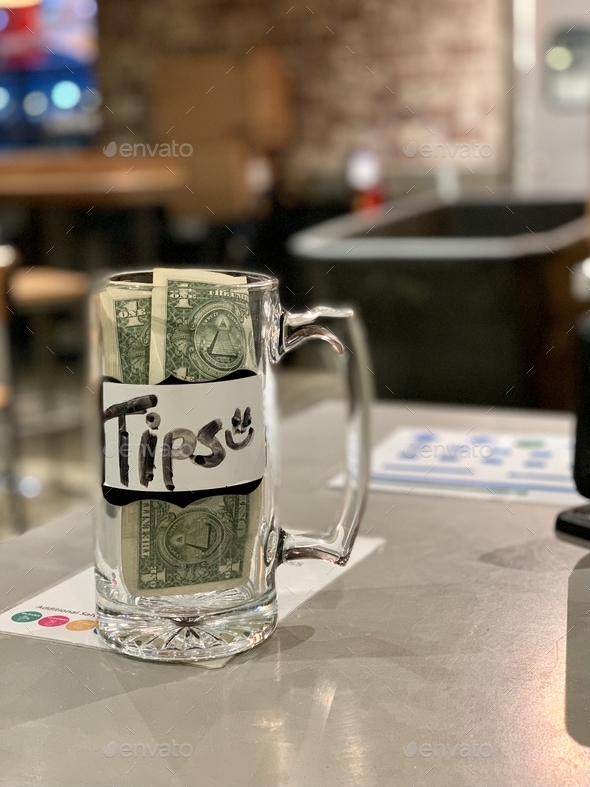 Tips glass jar at business next to cashier with money people leave as tips for workers.