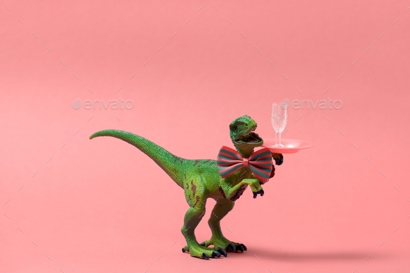 cute green toy dinosaur wearing bow tie and holding tray with wine glass on a pink background