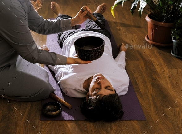 Woman making relaxing massage for young man. Meditation, sound therapy with Tibetan singing bowls.
