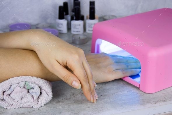close up of women\'s hand and nail polish drying lamp, manicure process in beauty salon