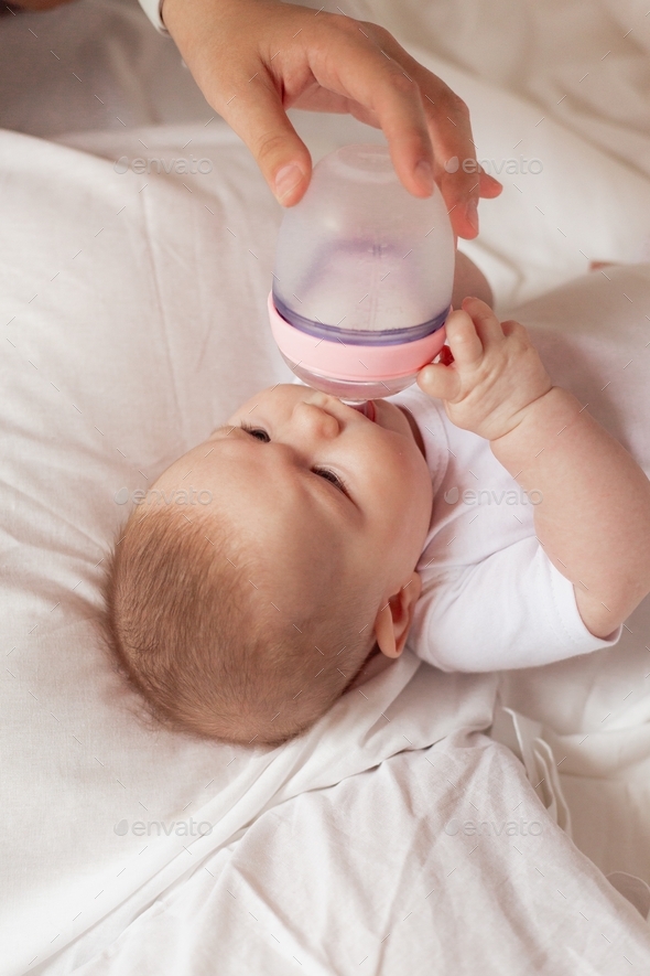 mom\'s or dad\'s hand gives bottle of milk or milk formula to newborn baby lying in bed. feeding baby