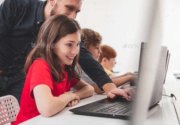 Happy schoolgirl with teacher working on laptop during lesson