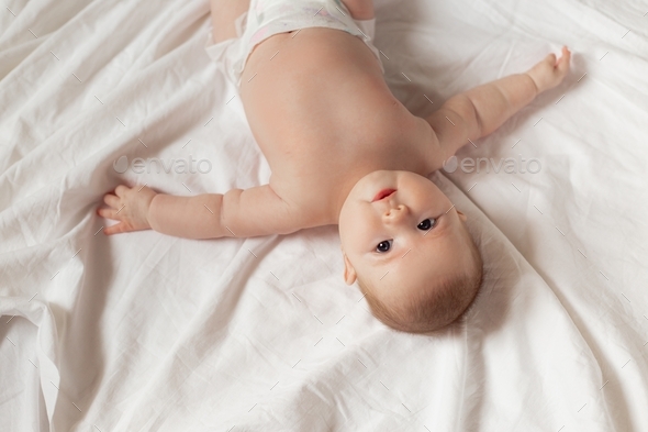 newborn baby in a diaper is lying on his back on a white sheet. products for children, toy