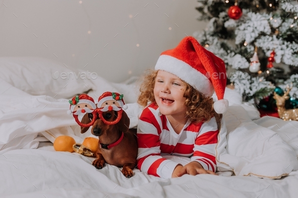 little girl in striped pajamas and a Santa hat and a dog in funny