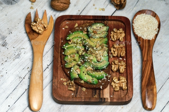 Sandwich with avocado, pepper, walnut and sesame seeds on a wooden board. Fork and spoon wooden.