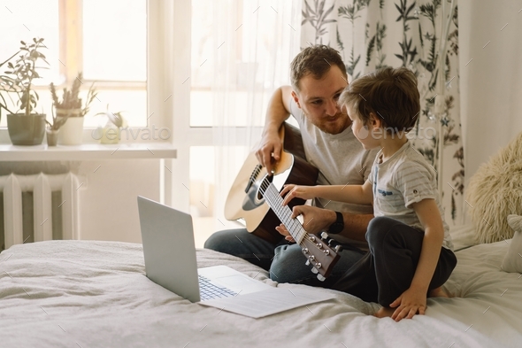 Father and son learn to play the acoustic guitar in an online lesson.