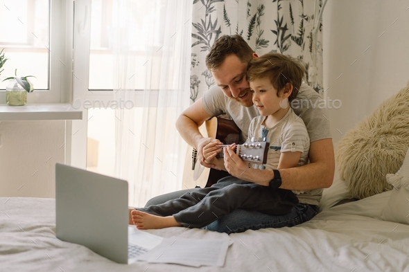 Father and son learn to play the acoustic guitar in an online lesson.