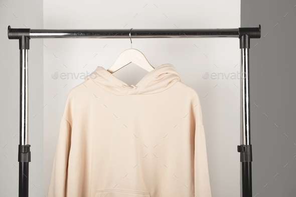 Blank beige unisex sweatshirt mockup on clothes hanger. Hoodie mock up in minimal interior.