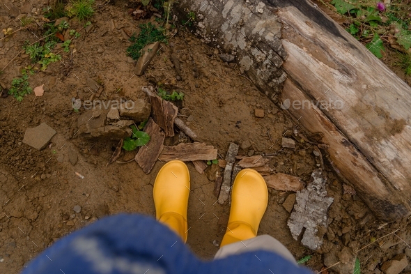 Female legs in yellow rubber boots while hiking in the mountains. Fall local trip.