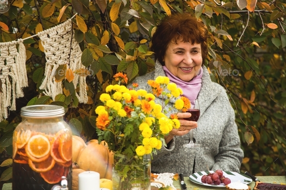 Elderly woman smiling drinking wine on fall brunch in the garden. Cottagecore style.