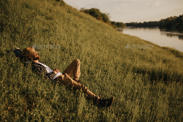 Male traveler resting on hill near river
