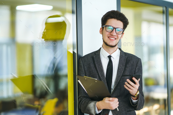 Young office worker in glasses using mobile smart phone. Businessman holds telephone in hand.