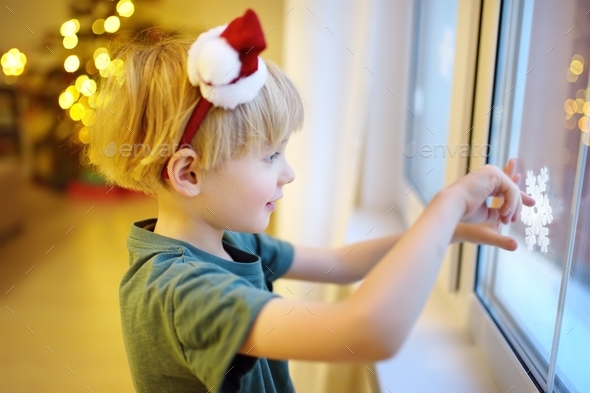 Little child getting ready for Christmas. Preschooler boy decorating home - attaching snowflake