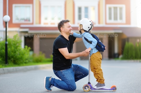 Little boy with scooter says goodbye and hugging to father before going to school