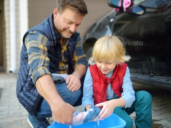 Preschooler boy helping his father washing family car. Little dad helper