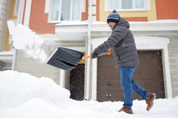 A mature man clean path near house from snow during strong blizzard