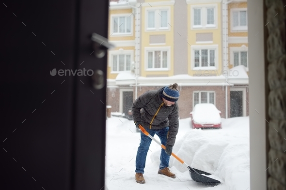 A mature man clean path near house from snow during strong blizzard