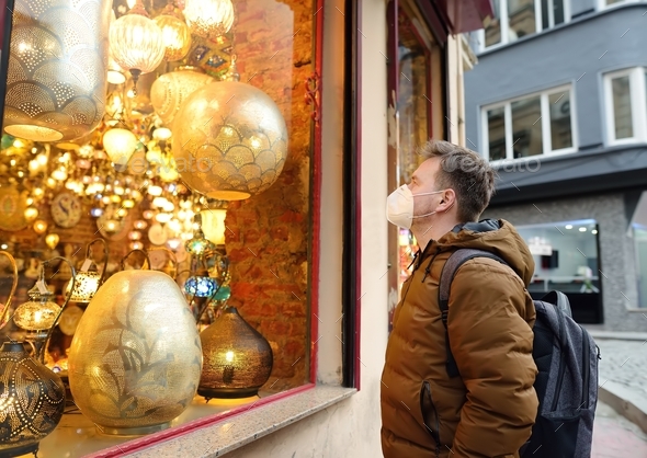 Man in face mask looking showcase of shop with exotic golden ottoman lamps on street of Istanbul