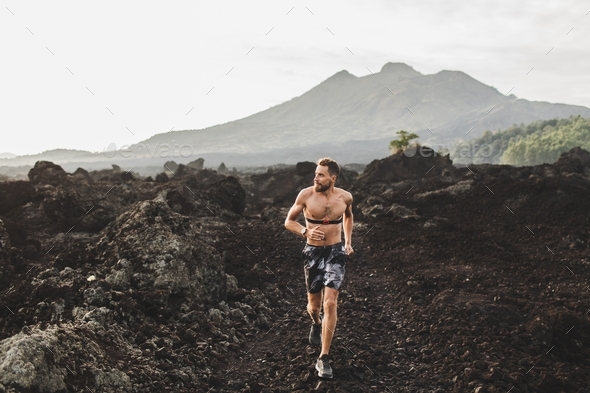 Young athletic man with beard trail running fast outdoors. Topless body and chest heart rate monitor