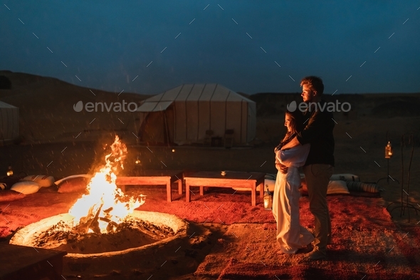 Couple hug in love near big campfire. Romantic night in glamping desert  camp in Sahara, Morocco Stock Photo by olegbreslavtsev