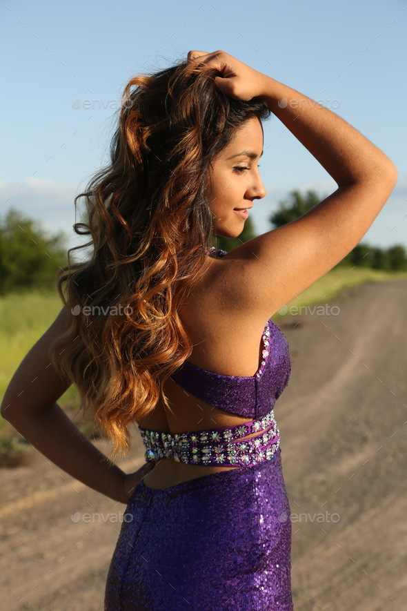Young woman in purple dress. Hands up on her hair. Elegant dress. Long hair. Prom dress.