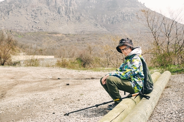 A teenager boy 11 years old goes hiking with hiking clothes, with trekking sticks, walks