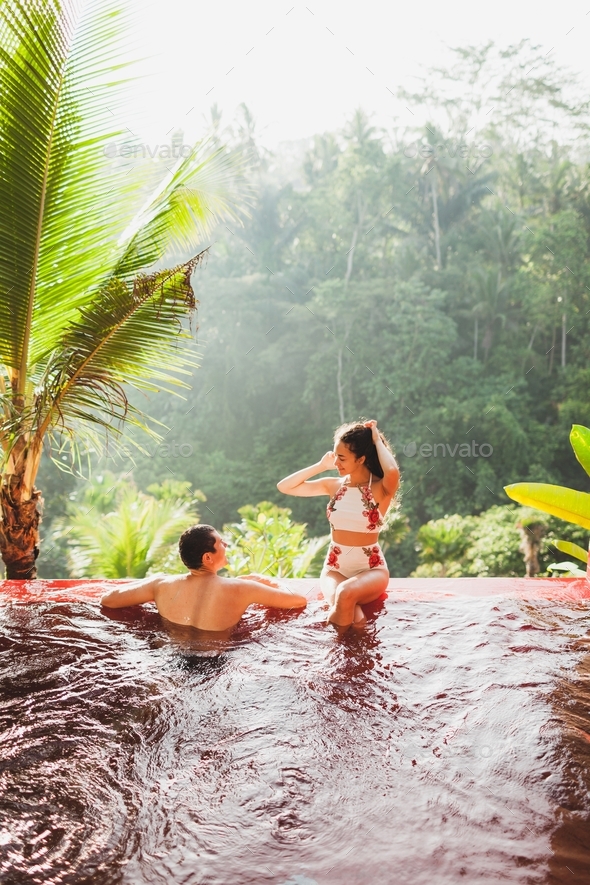 Young couple relaxing in luxury private infinity pool with amazing jungle view from above in Bali