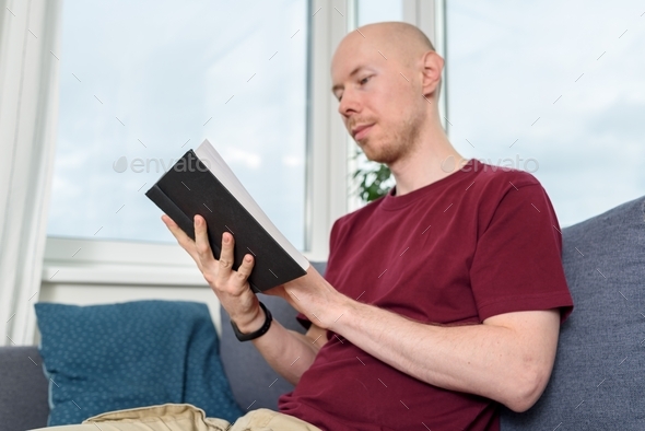 Bald man reading book on couch - Stock Photo - Images