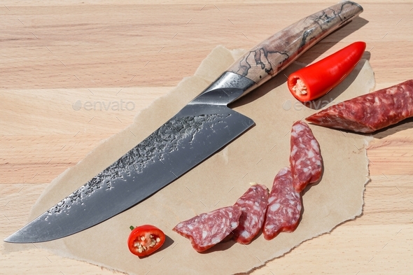 Sharp chef's knife close up on the cutting board and sliced smoked sausage. - Stock Photo - Images