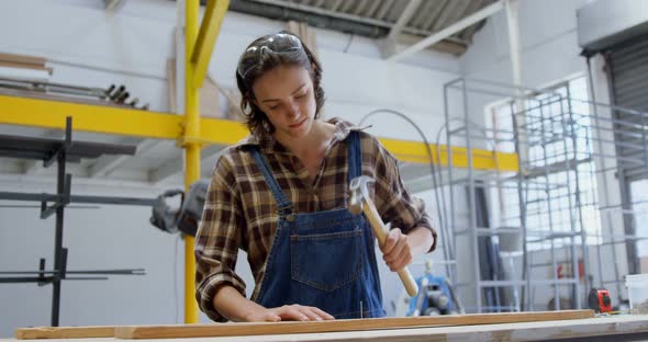 Female welder hammering nail on a wooden plank 4k alt