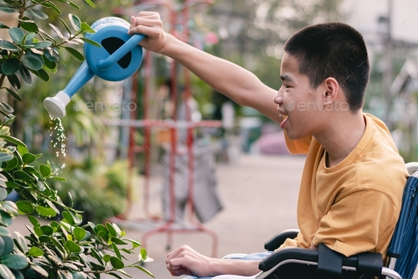 Happy disabled kid sitting on wheelchair watering the plants, environment friendly concept.