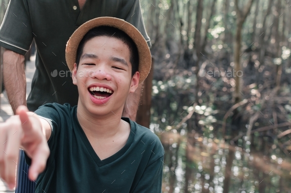 Asian special child on wheelchair pointing finger forward on mangrove forest background