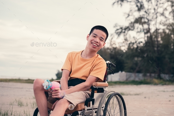 Handicapped teenager boy on wheelchair playing bubble gun on the beach.