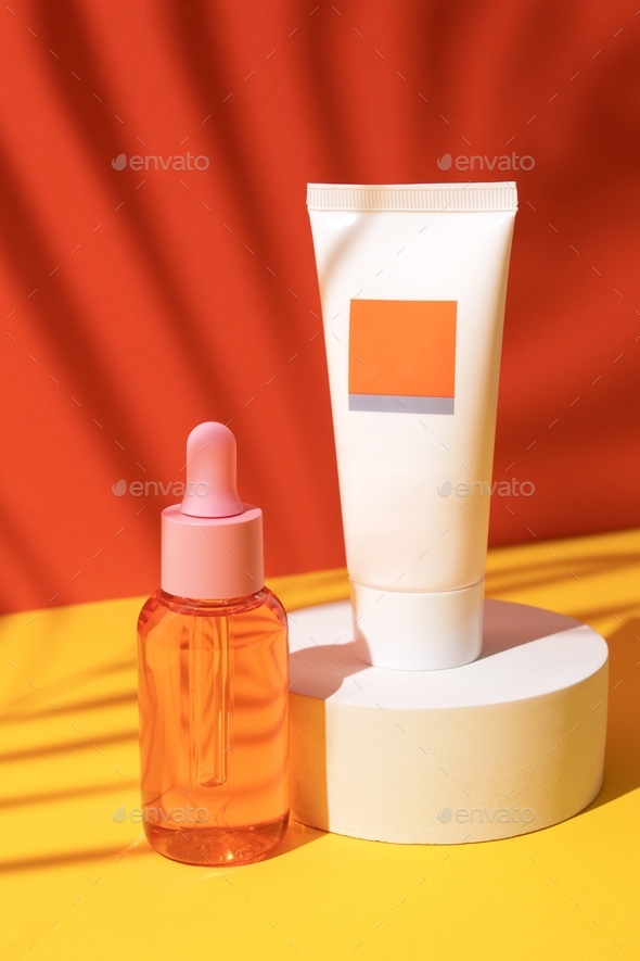Cosmetic bottle with oil and tube with cream on podium on orange background with palm leaves shadow.