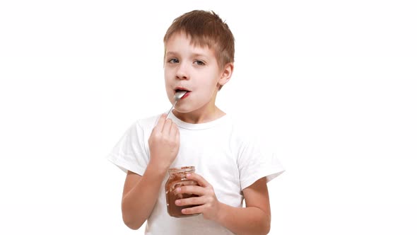 Elementaryschool Aged Caucasian Boy Eating Chocolate Spread with Great Pleasure Standing on White alt