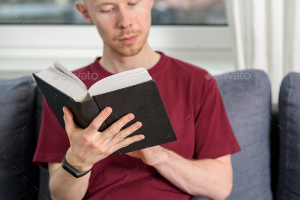 Bald man reading book on couch - Stock Photo - Images
