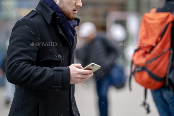 Attractive adult successful fashion man in black jacket using mobile phones on the city street